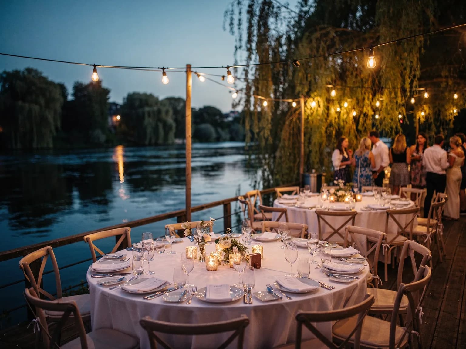 Reception tables set under string lights by a river at the end of the day — illustration