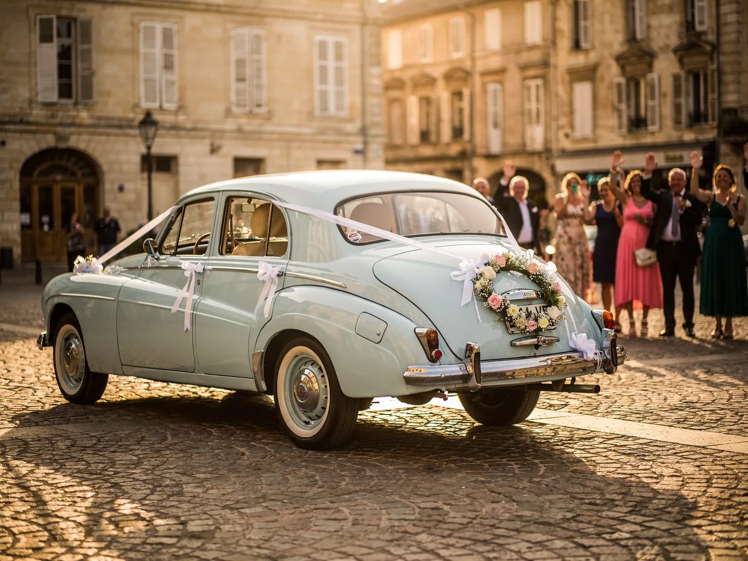 Voiture de mariage décorée quittant une place de centre-ville, invités saluant — illustration
