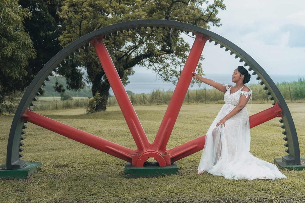 The bride in her white dress posing next to a large metal wheel